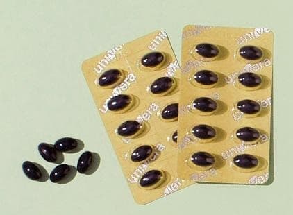 유니베라 글자가 새겨진 노란 PTP 블리스터 두 판과 낱개 검은 연질캡슐이 연두색 바닥에 놓인 컷