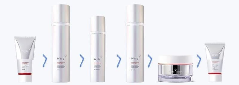W389 제품 여섯이 차례로 놓인 줄 — 필링젤 튜브, 토너 병, 스팟 에센스 병, 로션 병, 크림 단지, 선크림 튜브(은빛 · 빨간 띠). 사이사이 청보라 꺾쇠